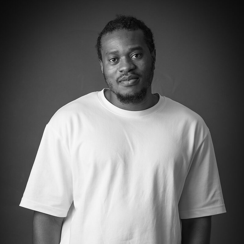 Black-and-white portrait of Dami Dare in a white T-shirt against a dark background